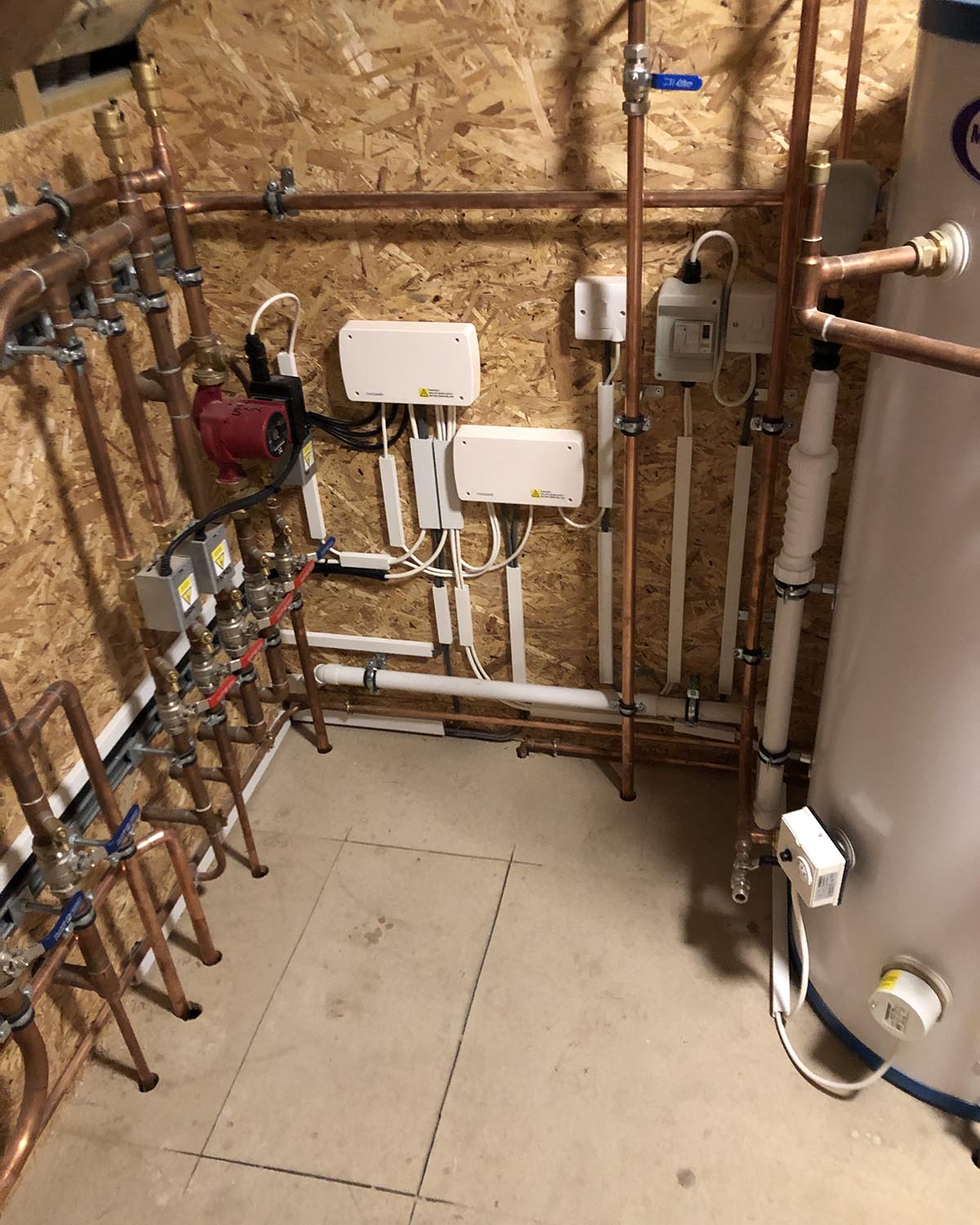 white boxes on wall with wirs and pipes, next to boiler. NBG Digital Home. Electric Vehicle chargers, Solar and Heat Pumps, General Electrical Services in the South West.