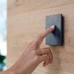 Hand touching black box on the wall to demonstrate using Loxone product. NBG Digital Home. Electric Vehicle chargers, Solar and Heat Pumps, General Electrical Services in the South West.